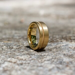 Puede incluir: Una banda de boda de color dorado con un acabado cepillado y un detalle acanalado.