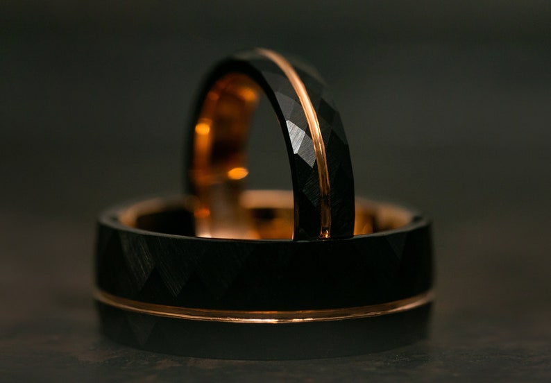 Puede incluir: Dos anillos de carburo de tungsteno negro con una incrustaci&oacute;n de oro rosa. Los anillos tienen un borde biselado y un acabado cepillado.