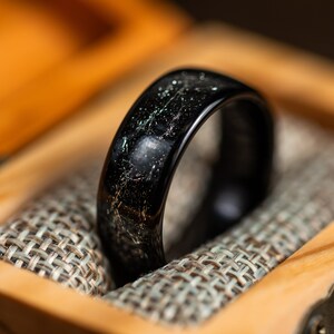 K&ouml;nnte beinhalten: Ein schwarzer Ring mit einem silbernen Streifen, der durch ihn verl&auml;uft, liegt in einer Holzschachtel mit Stoffauskleidung.