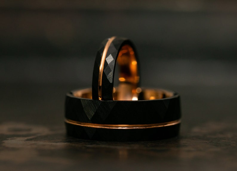 Puede incluir: Dos anillos de carburo de tungsteno negro con una banda de oro rosa. Los anillos tienen un acabado de corte de diamante.