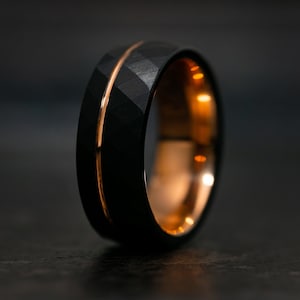 Puede incluir: Un anillo de carburo de tungsteno negro con una incrustaci&oacute;n de oro rosa. El anillo tiene un acabado cepillado y un borde biselado.