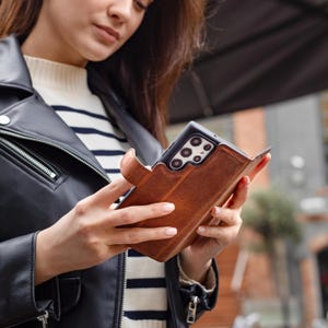 Puede incluir: Una funda de tel&eacute;fono de cuero marr&oacute;n con cierre magn&eacute;tico. La funda est&aacute; dise&ntilde;ada para guardar un smartphone y tiene una superficie texturizada. La funda del tel&eacute;fono se muestra en primer plano.