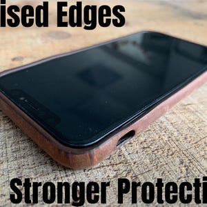 Peut inclure: Un smartphone dans une coque de protection en bois marron avec des bords sur&eacute;lev&eacute;s pour une meilleure protection. Le texte "Raised Edges" appara&icirc;t en haut &agrave; gauche et "Stronger Protection" en bas, soulignant la conception de la coque.