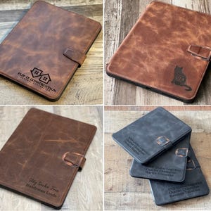 May include: Leather tablet cases in brown and gray with engraved designs and text. One case features the text "FLIP IT CONSTRUCTION", another has a cat silhouette, and others have personalized text.