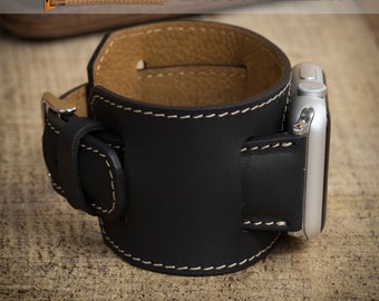 May include: Black leather Apple Watch cuff with white stitching and a silver buckle. The cuff has a tan interior and is designed to hold an Apple Watch. The text "I love you to the moon and back" is visible on the watch band. The words "PERSONALIZE IT!" are also visible.