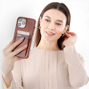 Peut inclure: Une coque de t&eacute;l&eacute;phone en cuir marron avec un porte-carte int&eacute;gr&eacute; &agrave; l'arri&egrave;re, contenant une carte Visa noire. La coque pr&eacute;sente une d&eacute;coupe pour le syst&egrave;me de triple objectif de l'appareil photo et recouvre le dos et les c&ocirc;t&eacute;s du smartphone.