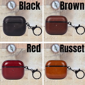 May include: Four square-shaped earbud cases with rounded corners, each featuring a black metal keychain ring. The cases are shown in black, brown, red, and russet colors, each labeled with its respective color name next to a small compass icon.