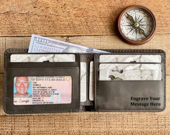 Puede incluir: Cartera de cuero marrón oscuro abierta con múltiples ranuras para tarjetas, una ventana de identificación transparente y un billete de cien dólares. También se ve una brújula vintage y el texto "Engrave Your Message Here".