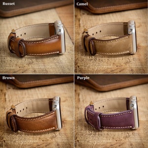 May include: Leather watch bands in russet, camel, brown, and purple. Each band features a contrasting interior, white stitching, and a silver watch case. The bands are displayed on a wooden surface.