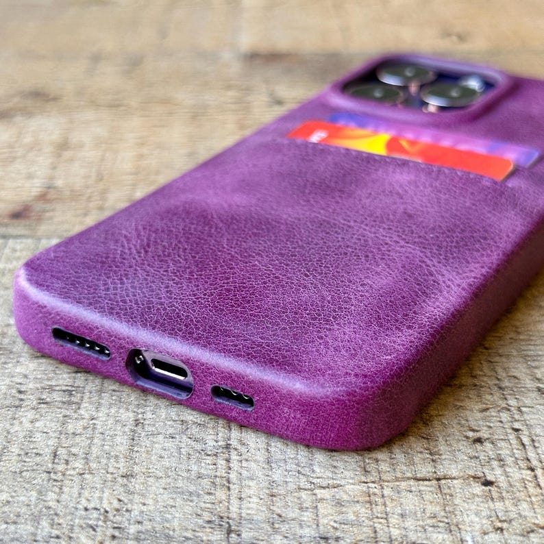 Peut inclure: Une coque de t&eacute;l&eacute;phone en cuir violet avec une surface textur&eacute;e et un porte-carte int&eacute;gr&eacute; au dos. L'&eacute;tui pr&eacute;sente des d&eacute;coupes pr&eacute;cises pour les objectifs de l'appareil photo en haut et pour le port de charge et les haut-parleurs en bas.