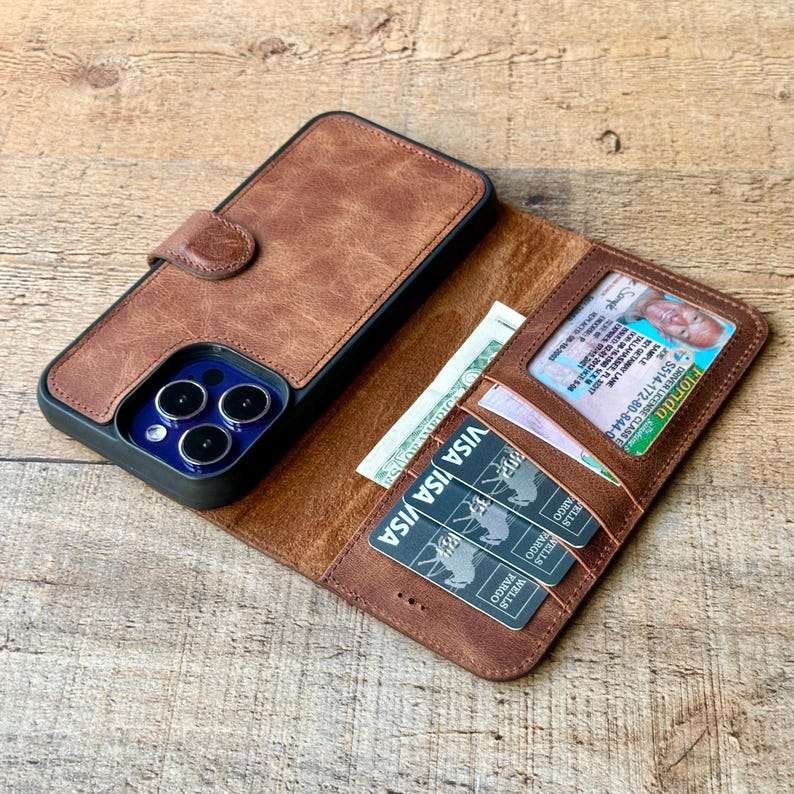 Puede incluir: Funda de tel&eacute;fono de cuero marr&oacute;n con funci&oacute;n de cartera. La funda est&aacute; abierta, revelando una licencia de conducir, dinero en efectivo y varias tarjetas de cr&eacute;dito. La funda es marr&oacute;n con borde negro y cierre magn&eacute;tico.