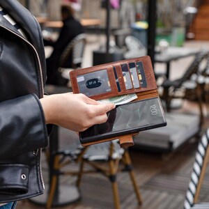K&ouml;nnte beinhalten: Eine braune Ledergeldb&ouml;rse mit mehreren Kartenf&auml;chern und einem Handy-Etui. Die Geldb&ouml;rse ist ge&ouml;ffnet und eine Kreditkarte und Bargeld sind sichtbar.