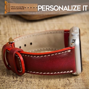 以下が含まれることがあります： 白ステッチとシルバーの文字盤が付いた、バーガンディ色の革製腕時計バンド。 バンドは赤いエッジとバックル留めです。 上部のテキストは「I love you to the moon and back」と「PERSONALIZE IT」です。