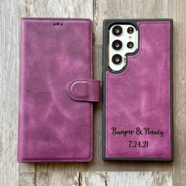 K&ouml;nnte beinhalten: Eine Handyh&uuml;lle aus lila Leder mit schwarzem Rahmen und einer Klappe, die mit einem Knopf geschlossen wird. Die H&uuml;lle tr&auml;gt den Text "Bumper & Nancy 7.24.21" auf der R&uuml;ckseite.