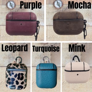 May include: Five protective cases for wireless earbuds, each featuring a black carabiner clip. The colors include purple, mocha, leopard print, turquoise, and mink. Each case has a distinct texture and black trim, with labels identifying each color.