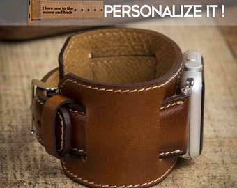 May include: A brown leather Apple Watch cuff with white stitching and a silver buckle. The watch band has the text "I love you to the moon and back" and the words "PERSONALIZE IT!" are displayed in white.