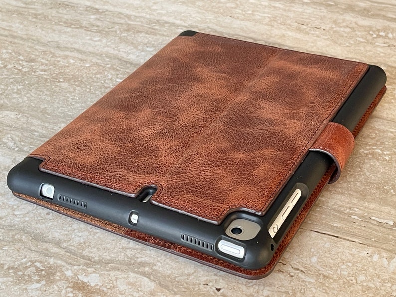 May include: A brown leather tablet case with a textured finish. The case has a magnetic closure and a black frame. The tablet case is designed to protect the device from scratches and damage.