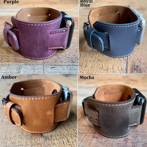 Puede incluir: Correa de reloj de cuero en cuatro colores: morado, azul real, &aacute;mbar y moca. Cada correa presenta un dise&ntilde;o de brazalete con cierre de hebilla y costuras blancas. Las correas de reloj se muestran sobre una superficie de madera.