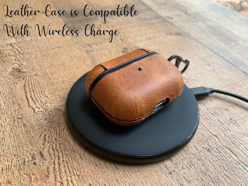 May include: A tan leather protective case for wireless earbuds resting on a black circular wireless charging pad. The text "Leather Case is Compatible With Wireless Charge" is visible in the upper left corner of the image.