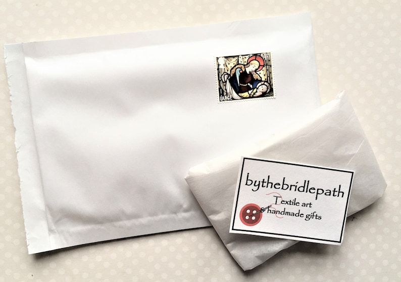 Puede incluir: Un sobre acolchado blanco con un sello que muestra una imagen religiosa. El sobre est&aacute; etiquetado con "bythebridlepath Textile art & handmade gifts".