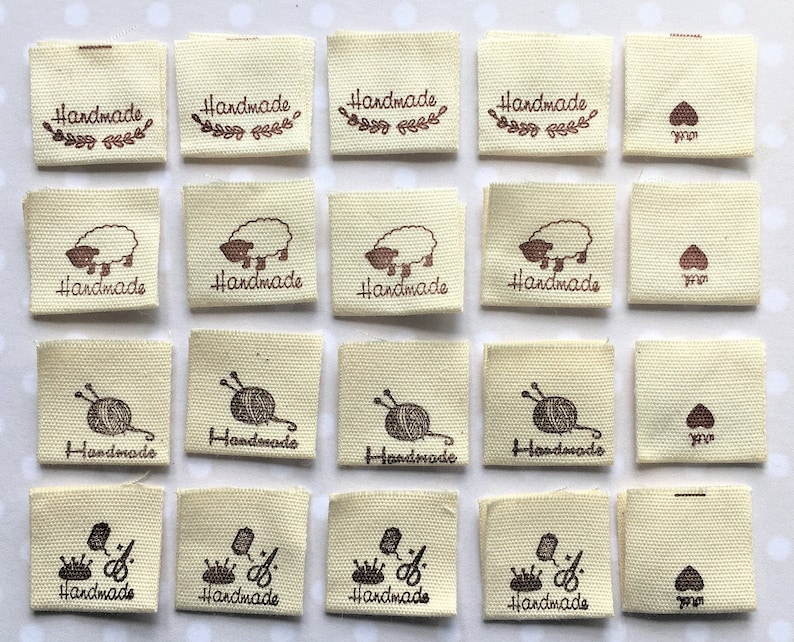 K&ouml;nnte beinhalten: Vierundzwanzig beigefarbene Stoff-Etiketten mit braunen Druckdesigns. Die Designs beinhalten ein Schaf, eine Wollkn&auml;uel mit Stricknadeln, eine Krone mit einer Schere und ein Herz. Die Etiketten sagen "Handmade".