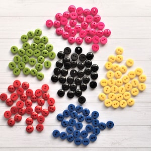 May include: Assortment of colourful plastic buttons in red, green, yellow, blue and black. The buttons are two-hole and have a smooth, shiny finish.
