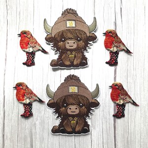May include: Embroidered patches of a cartoon Highland cow wearing a brown hat and plaid shirt, and red robins in polka dot wellington boots. The patches are set against a light wood grain background.