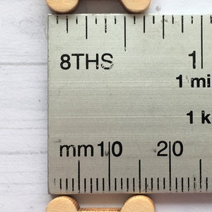 May include: Two wooden bone-shaped buttons with two holes each. The buttons are light brown and measure approximately 1 inch in length.
