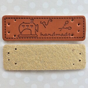 May include: Brown leather label with a sewing machine, scissors, and the word "handmade" embossed on it. A blank beige leather label is also shown.