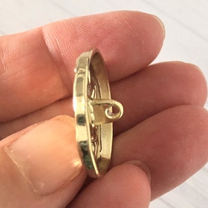 May include: A gold-toned metal button with an intricate design. The button has a loop on the back for sewing.