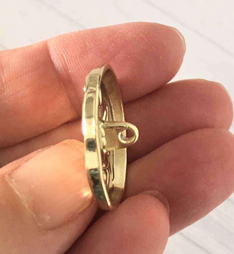 May include: A gold-toned metal button with an intricate design. The button has a loop on the back for sewing.
