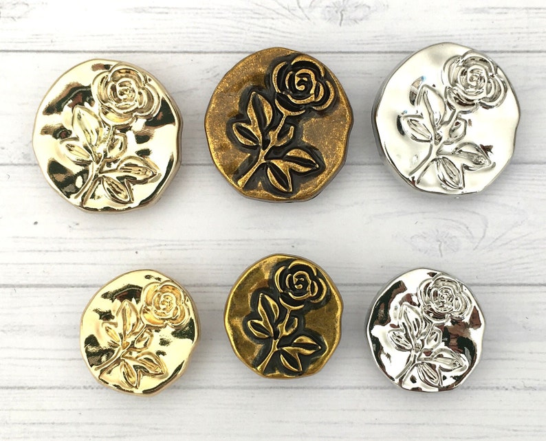 May include: Six decorative buttons with a rose design. The buttons are made of metal and have a gold or silver finish. The roses are embossed and have a three-dimensional effect.