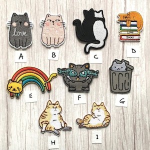 May include: Nine embroidered iron-on patches featuring various cat designs. The patches include a cat with a rainbow, a cat with fish, a cat in a bin, a cat with the word "love", a cat reading books, and several other cats.