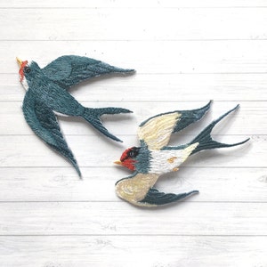 May include: Two embroidered swallow bird patches. One is teal blue and white, the other is yellow, white, and teal blue.