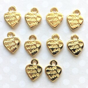 May include: A collection of ten gold-colored heart-shaped charms. Each charm has a loop at the top for attachment and the words "Made With Love" embossed on the front. The charms are suitable for jewelry making or craft projects.