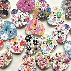 May include: Assortment of heart-shaped wooden buttons with various floral and butterfly patterns. The buttons are in shades of pink, blue, green, and white.