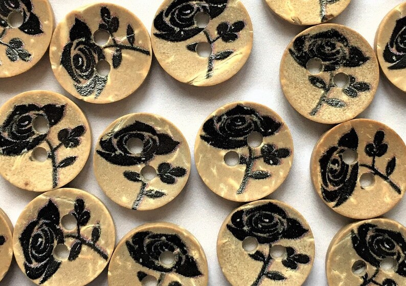 Puede incluir: Una colecci&oacute;n de 12 botones de madera con un dise&ntilde;o de rosa negra. Los botones son beige con una superficie ligeramente texturizada. Cada bot&oacute;n tiene dos agujeros.