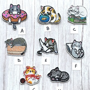 May include: Set of 9 embroidered iron-on patches featuring cute cats in various poses. The patches include a cat in a doughnut, a cat with a fishbowl, a cat reading books, a cat sleeping on a cake, a cat playing with yarn, a cat sleeping on a pillow, a cat sleeping on a bed, a cat playing with a ball of yarn, and a cat sleeping on a bed.