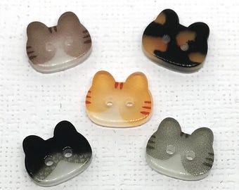 May include: Five cat-shaped buttons in various colors: brown, black, orange, gray, and calico. Each button has two holes for sewing and a glossy finish. The buttons are designed to resemble cat faces.