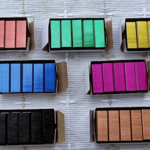 May include: Eight boxes of staples in different colors: red, green, gold, blue, pink, black, and brown. Each box contains six staples.