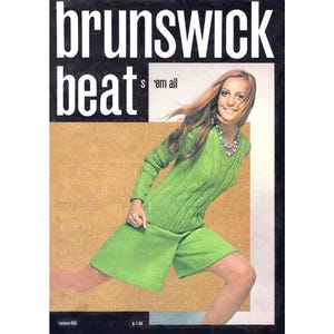 May include: Magazine cover featuring a woman in a green knit sweater and shorts. The magazine title "brunswick beat" is in large white letters. The woman is wearing a colorful necklace and smiling. The background is a textured tan color.
