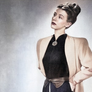 May include: A woman wearing a black and white top with a jeweled brooch, a brown jacket, and a brown belt.