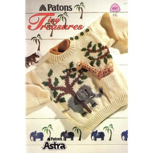 May include: A cream colored knitted sweater with a brown tree, green leaves, a gray elephant, and a brown giraffe. The sweater has a button closure and a pocket on the front. The sweater is on a white wooden background with palm trees and elephants printed on it. The text "Patons Tiny Treasures" is at the top of the image. The text "Patons Astra" is at the bottom of the image.