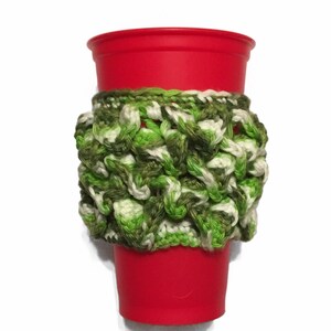 Puede incluir: Un calientavasos de ganchillo verde, blanco y marrón en una taza roja.