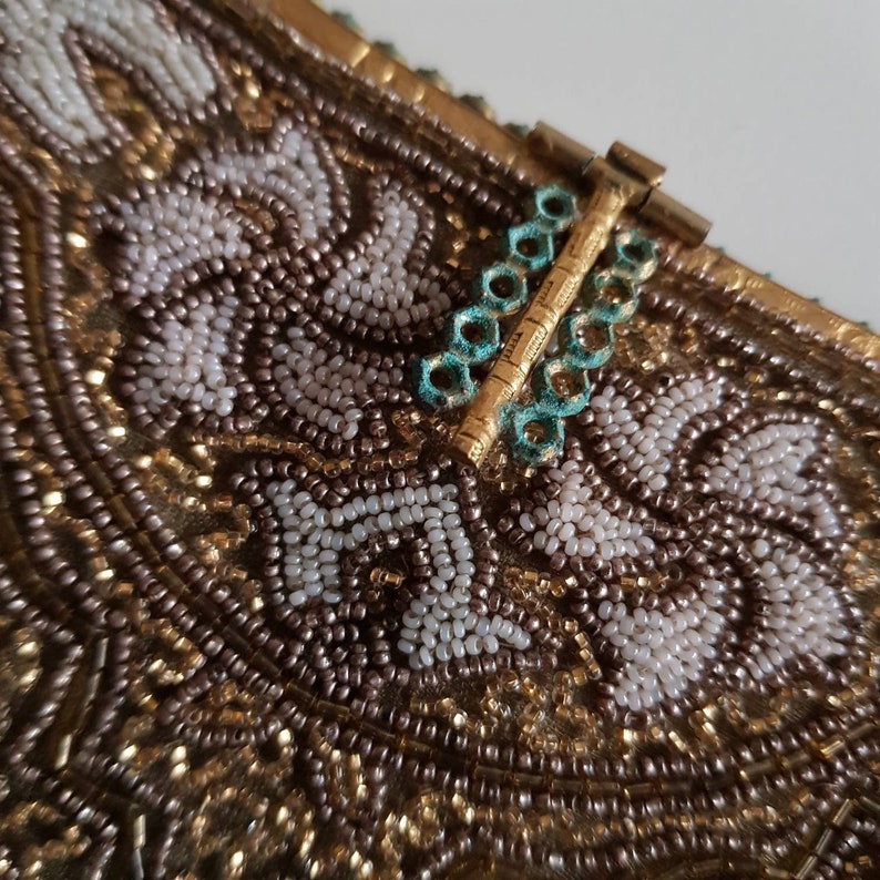 May include: Close-up of a vintage beaded handbag. The bag features intricate beadwork in gold, white, and brown tones, with a floral pattern. The clasp is gold with turquoise accents, adding a touch of colour to the design.