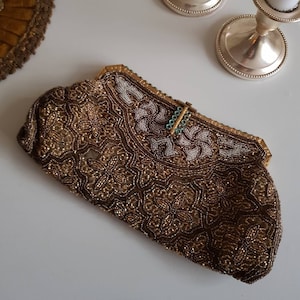 May include: A vintage beaded clutch bag in brown and gold, with detailed floral patterns. The top section has white beading and a gold frame with a turquoise clasp. A decorative item for special occasions.