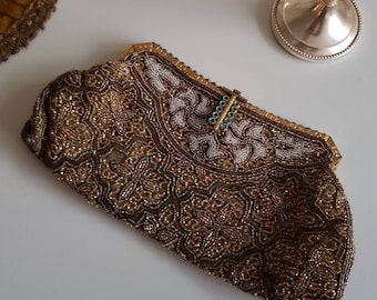 May include: A vintage beaded clutch in shades of brown and gold, with intricate floral patterns. The top section features white beading and a gold frame with a turquoise clasp. A decorative item for special occasions.