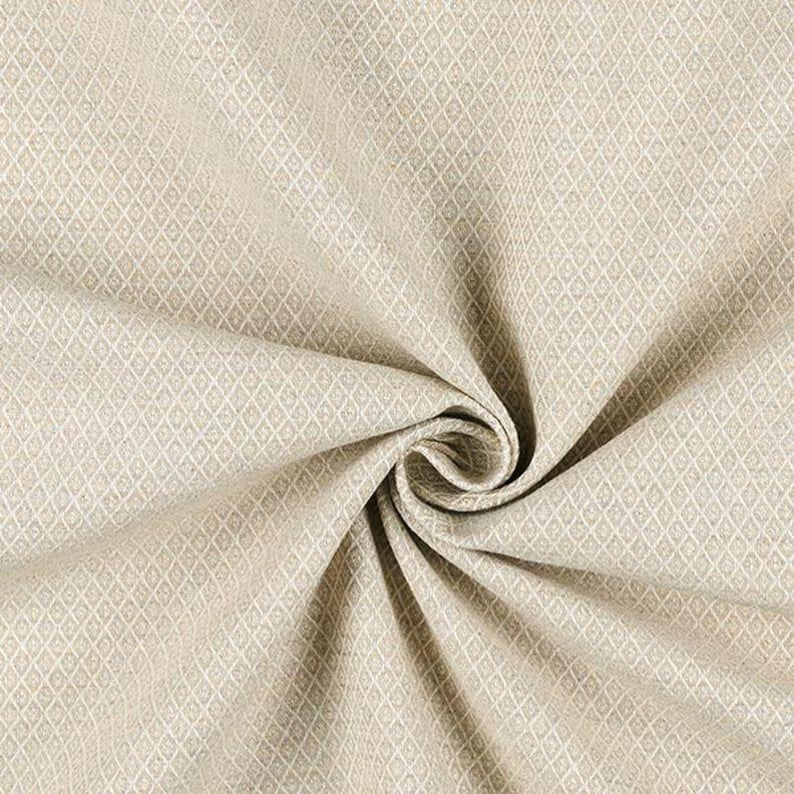 Puede incluir: Primer plano de una tela beige con un patr&oacute;n de diamantes. La tela est&aacute; doblada y arremolinada, mostrando su textura y dise&ntilde;o. El color neutro y el patr&oacute;n sugieren su uso para tapicer&iacute;a o decoraci&oacute;n del hogar.