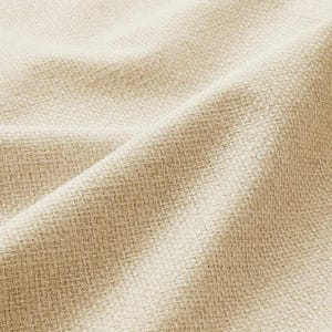 Può includere: Primo piano di un tessuto intrecciato con una superficie strutturata. Il tessuto è di colore beige chiaro, con un motivo sottile creato dall'intreccio. Le pieghe e le ombre aggiungono profondità all'immagine.