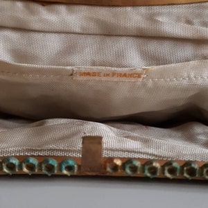 May include: Close-up of the interior of a vintage handbag. The lining is a light beige fabric. The gold-toned frame is embellished with turquoise-coloured accents. The label inside reads "MADE IN FRANCE".